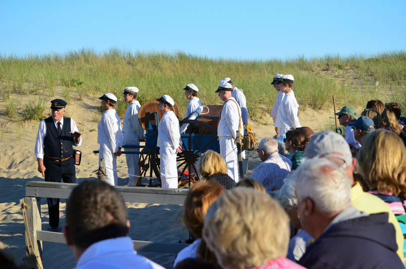 Park staff and volunteers stand around a cannon as visitors look on.