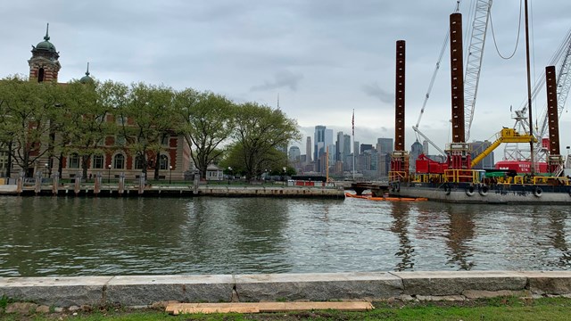 A view of the main building on Ellis Island with a construction barge.