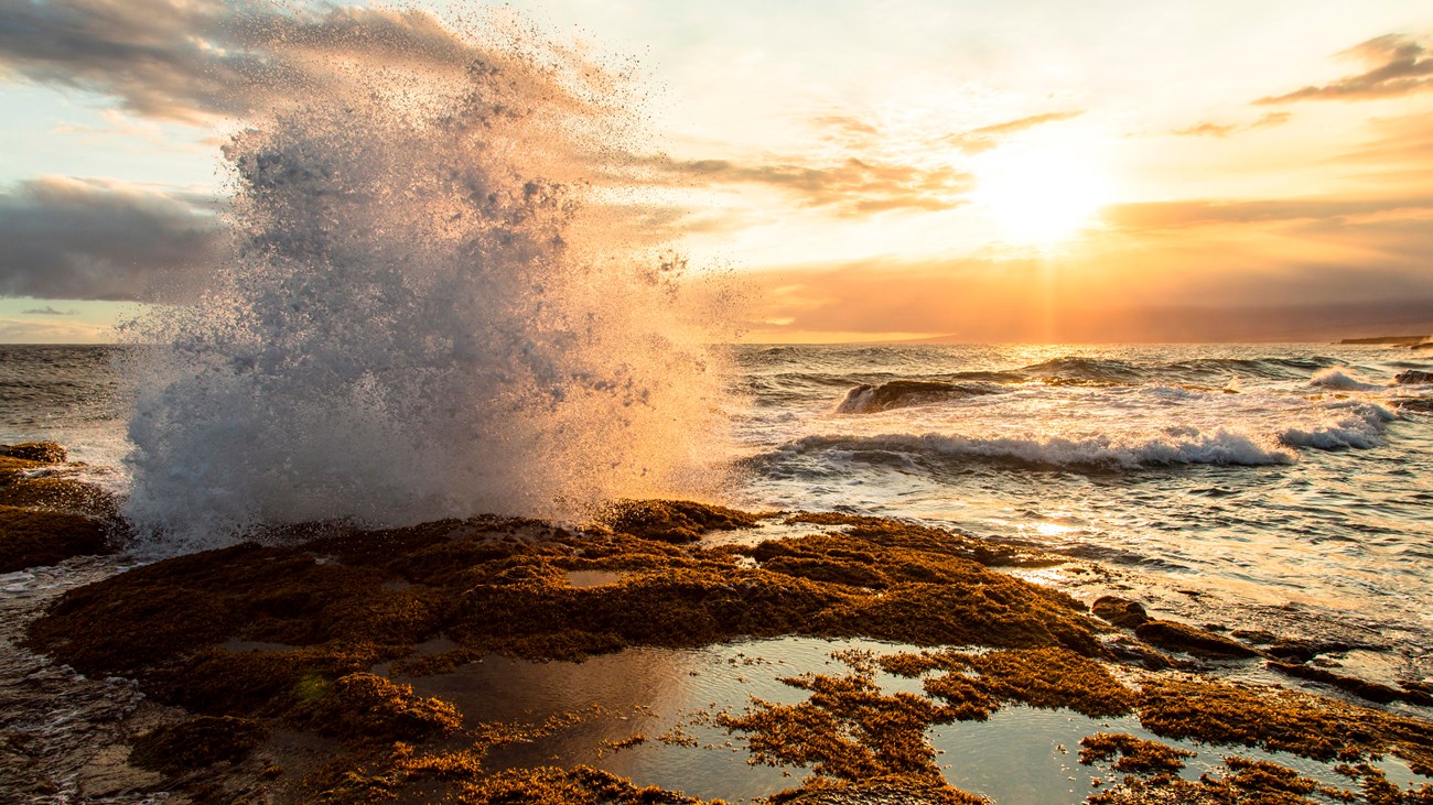 Waves crashing on rocks near tidal pools at sunset