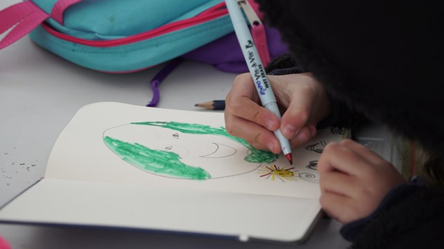 Close-up of child's hand holding marker, drawing in journal.