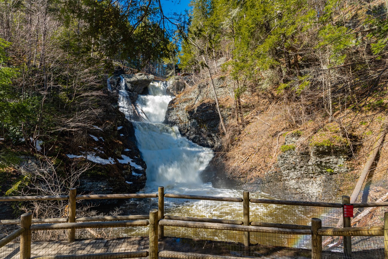 Water roars over the edge of Raymondskill Falls sending up mist that reflects the light like a rainbow