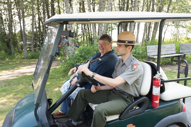 Two people, one in an NPS uniform, riding in a golf cart.