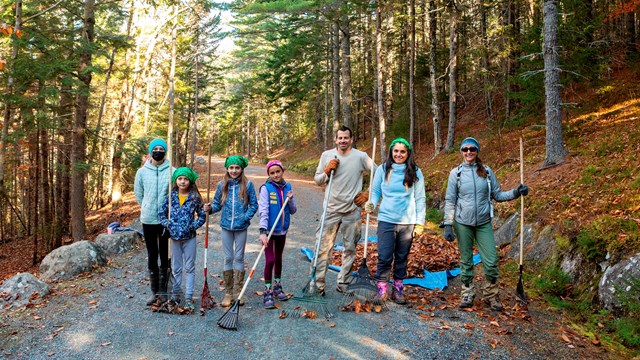 People standing in a carriage road holding rakes and tools