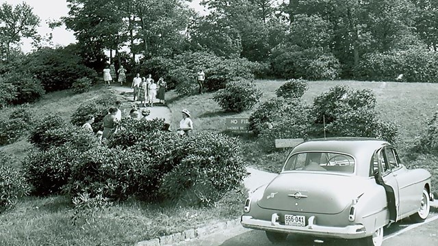 A mid-1900s automobile parked beside a busy hiking trail