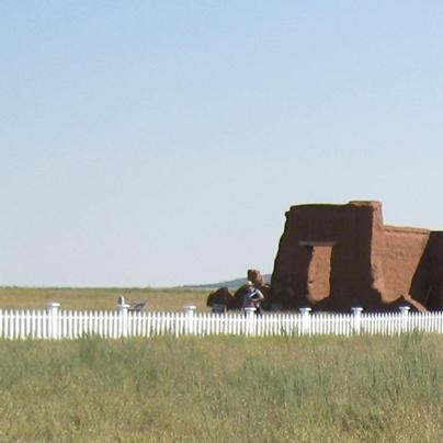 Two signs in front an adobe fort and blue sky