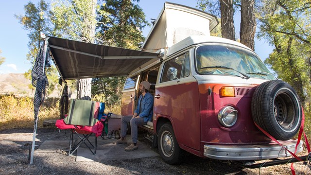 Visitor sitting in a vintage red bus RV taking in the view of the Teton Range.