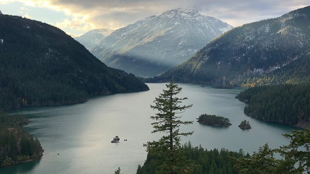 A blue lake surrounded by forested, snowy mountains.