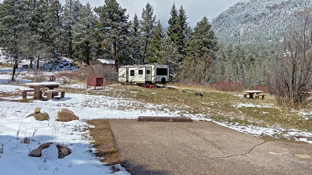 A view of a campsite in Aspenglen Campground with an RV parked. The campsite has snow on the ground