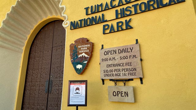 front entrance of visitor center with hours, fees, and COVID mask signage