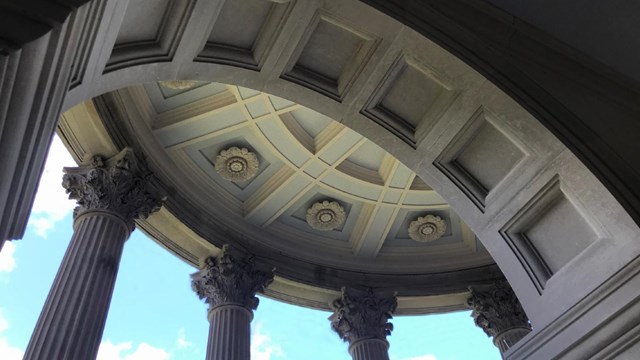 A view through a limestone arch to a pair of columns supporting a portico.