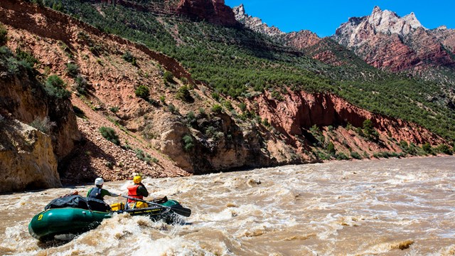 A green raft crashes through a wave in a rapid.