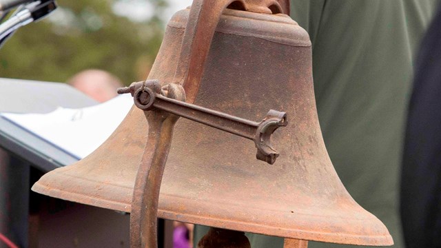 A large bell stands next to a speaker's podium.