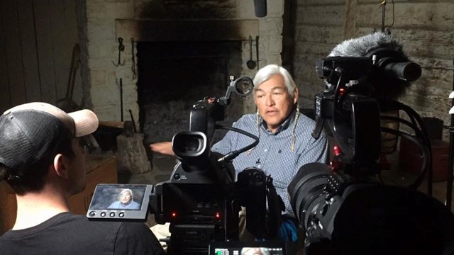 Man interviewing facing camera, second man watching playback on two small video screens.