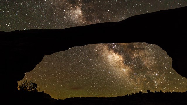 a massive stone arch with the Milky Way and stars overhead