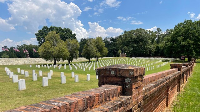 Rows of marble headstones in turf in a national cemetery, surrounded by a masonry wall