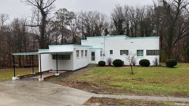 Photograph of Azurest South, a one-story house with carport and trees in the background.