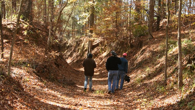 A wide sunken trail with people walking on it. 