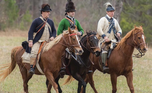 Reenactors stand next to a fire. 