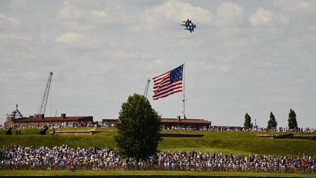 fighter jets fly over a fort with crowd below