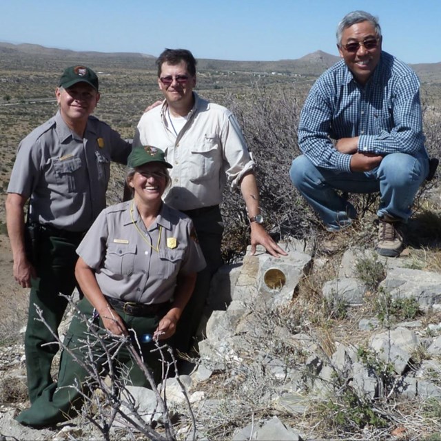 4 people sitting on a rock outcrop in the desert