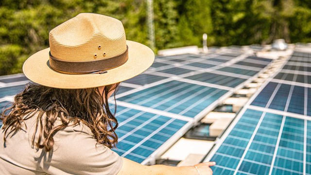 A park ranger points to solar panels. 