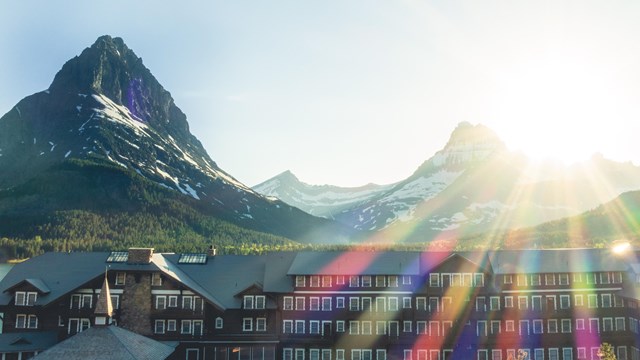 A large hotel sits next to a lake with mountains behind. 