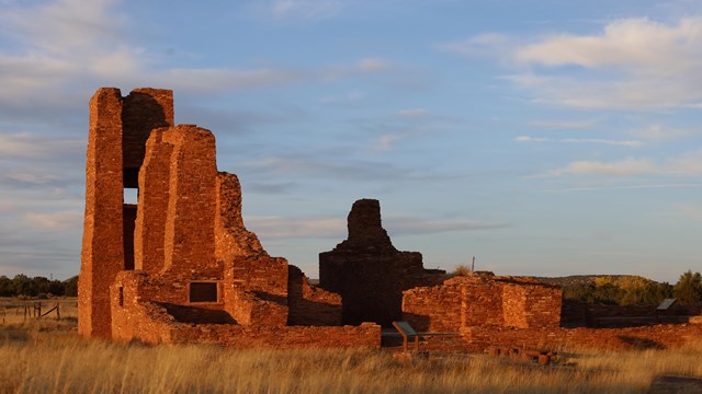 Red sandstone church ruins lit orange at sunset.