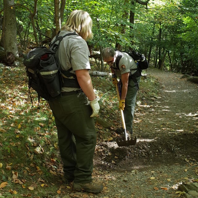 Uniformed trail worker leaning down to dig water ditch