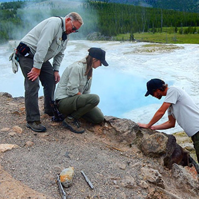 Three people work on the side of a pathway, water in the background