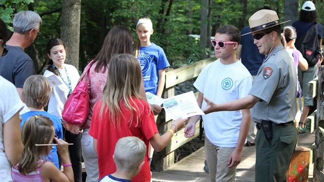 A ranger and other seasonal employees take tickets from a family heading over a bridge