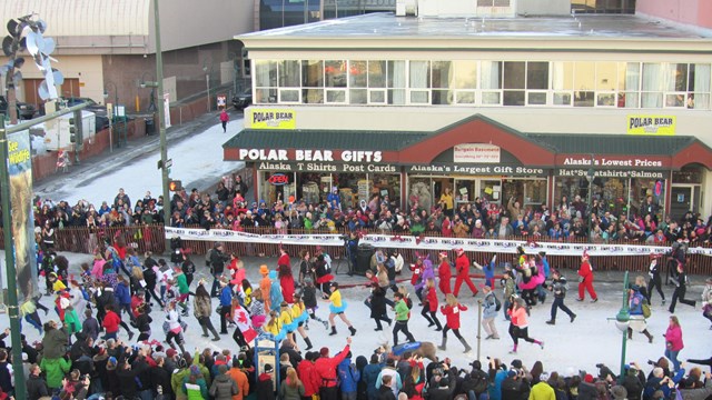 Outdoors; looking down from a height upon a crowd lining both sides of a street with runners on it..