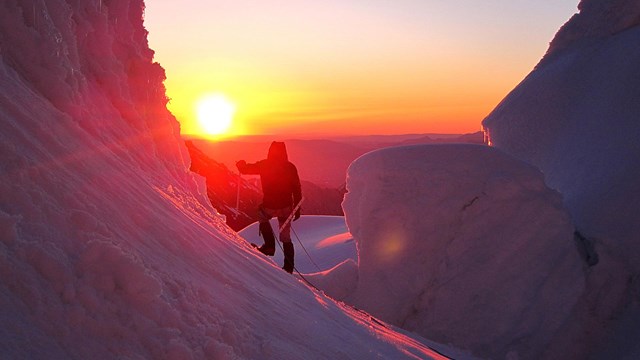 mountaineer on a snowy mountain backlit by a setting sun