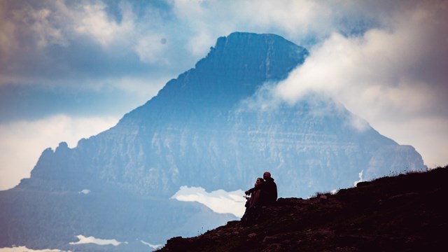 A small group of people sit on a hill with a mountain peak in the background. 