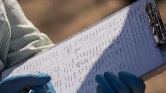 Hands wearing gloves writing on form on clipboard