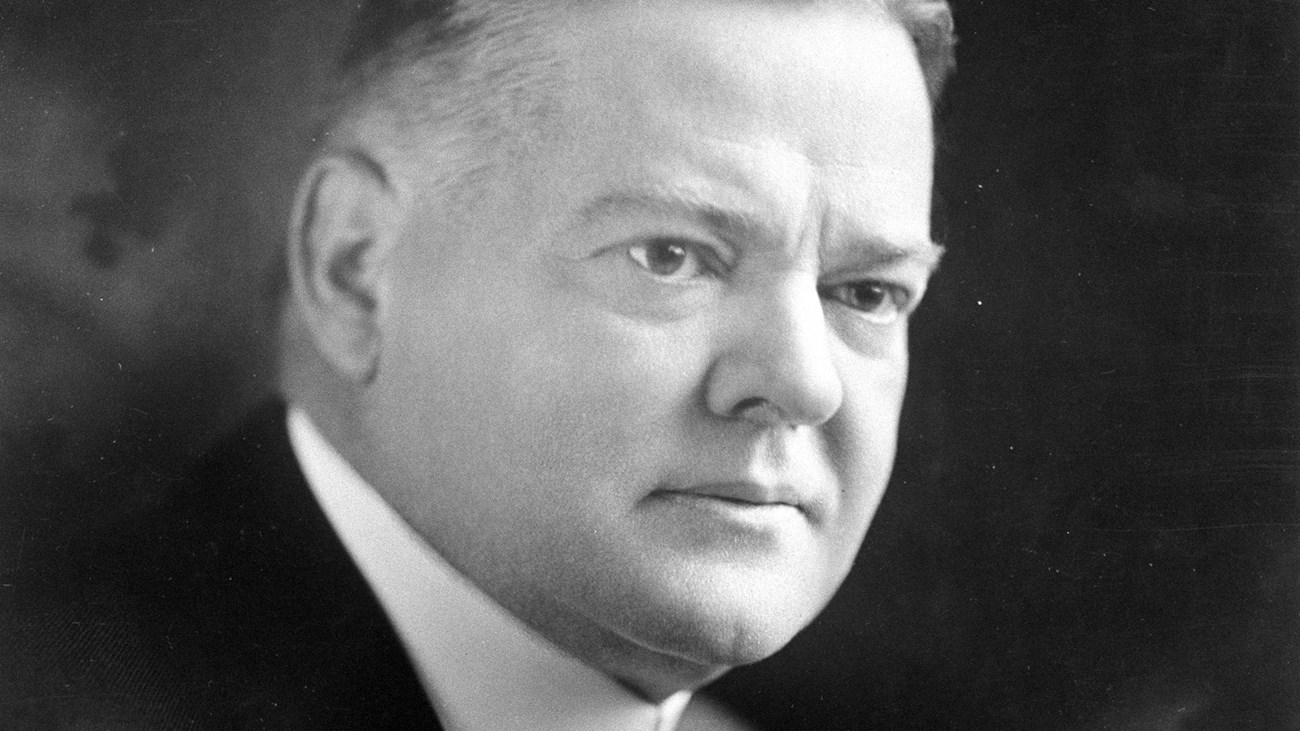 A middle aged man in a suit, tie, and high-collar shirt sits for a portrait photo.