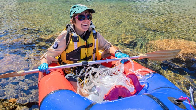 Person sharing a small inflatable boat with a pile of water sampling equipment.