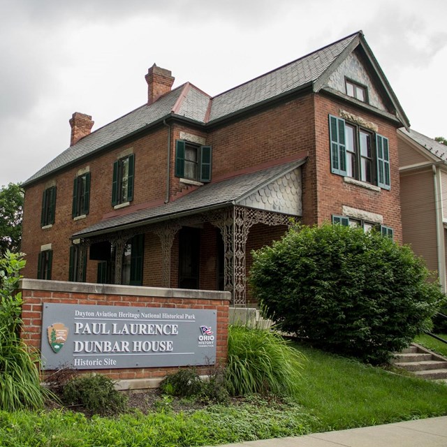 Two-story brick house with a sign in front reading 