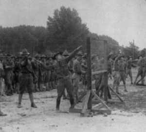 A soldier throws a hand grenade over an obstacle while other troops observe.