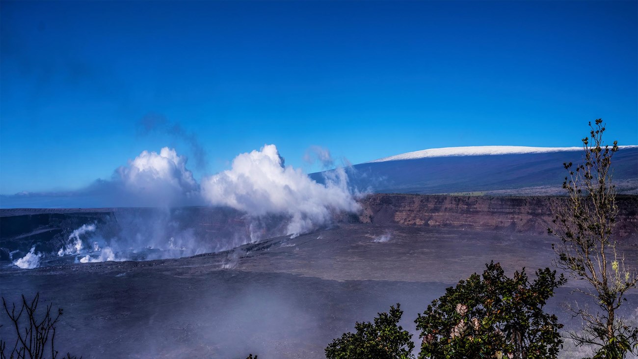 A steaming crater and a snow-capped volcano in a distance. 