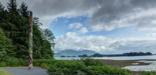 Two totem poles overlook spruce and hemlock forest, tidal flats and ocean.