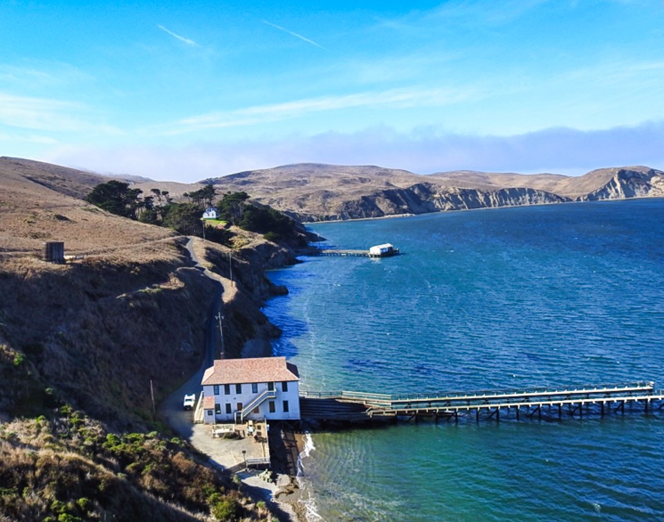 A black and white photo of buildings and piers on a steep hillside on the left with a bay filled with boats on the right.