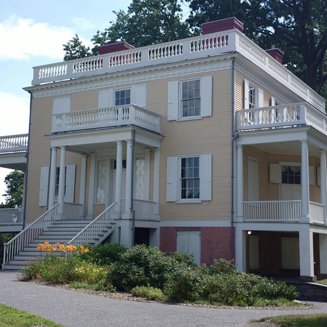 A cubicle, yellow, two-story building. It has white porches and railings on all sides. 