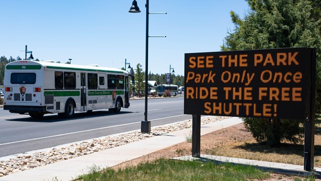 A shuttle drives past a sign that has information about the free shuttle service.