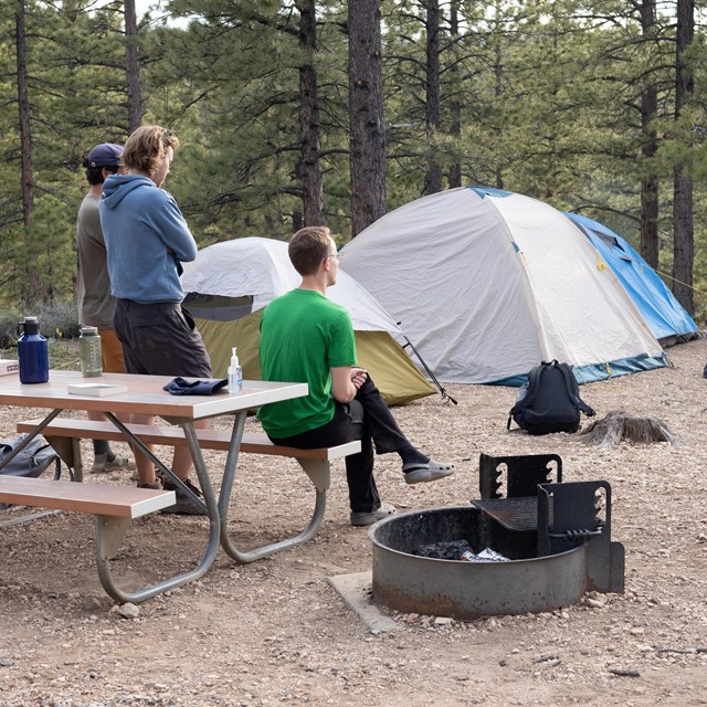 People sit at a picnic table with a tent in the background.