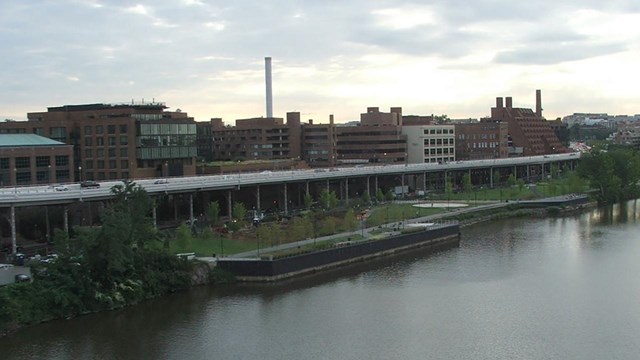 River, park and city skyline below a sky with patchy clouds.