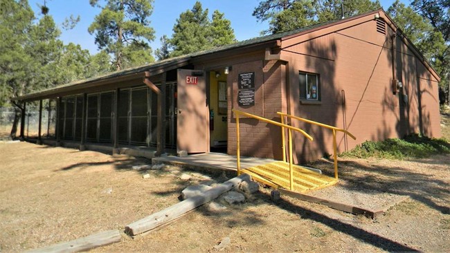 A brown single story building with a row of 10 screen doors for individual dog rooms.