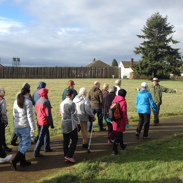 Several people walking on a dirt path with a large timber fort in the background