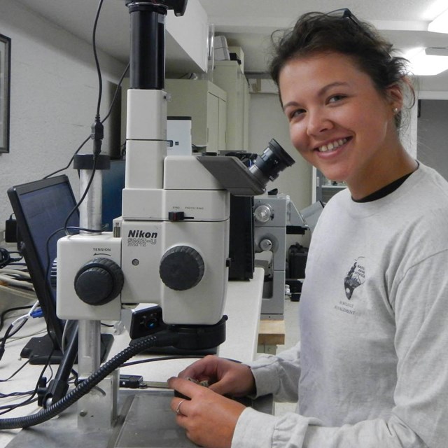 A woman stands next to a microscope