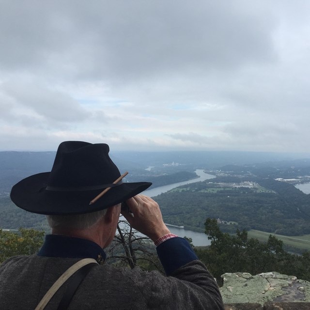 A soldier in Union uniform looks through binoculars from a height.