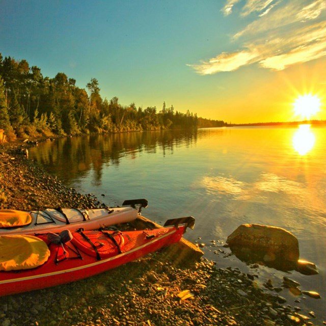 two canoes rest along the wooded bank of a lake in the setting sun